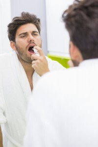 Reflection of man spraying medicine in mouth