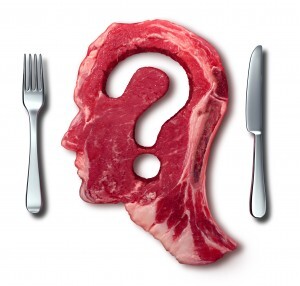 Eating meat questions concept or diet and nutrition decisions as a red steak with a question mark cut out of the raw food with a dinner table setting with a fork and knife as a symbol of menu uncertainty.